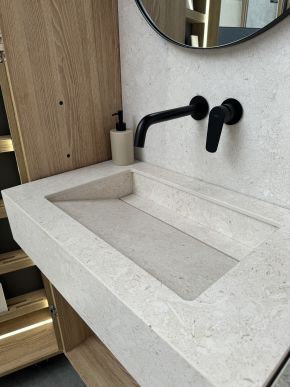 Heller Waschtisch mit rechteckigem Becken, schwarzer Wandarmatur, runder Spiegel und Holzverkleidung im Hintergrund.