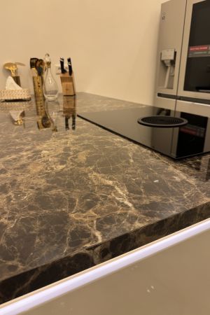 Moderne Küche mit glänzender, dunkel marmorierter Arbeitsplatte, Induktionskochfeld und silbernem Kühlschrank.