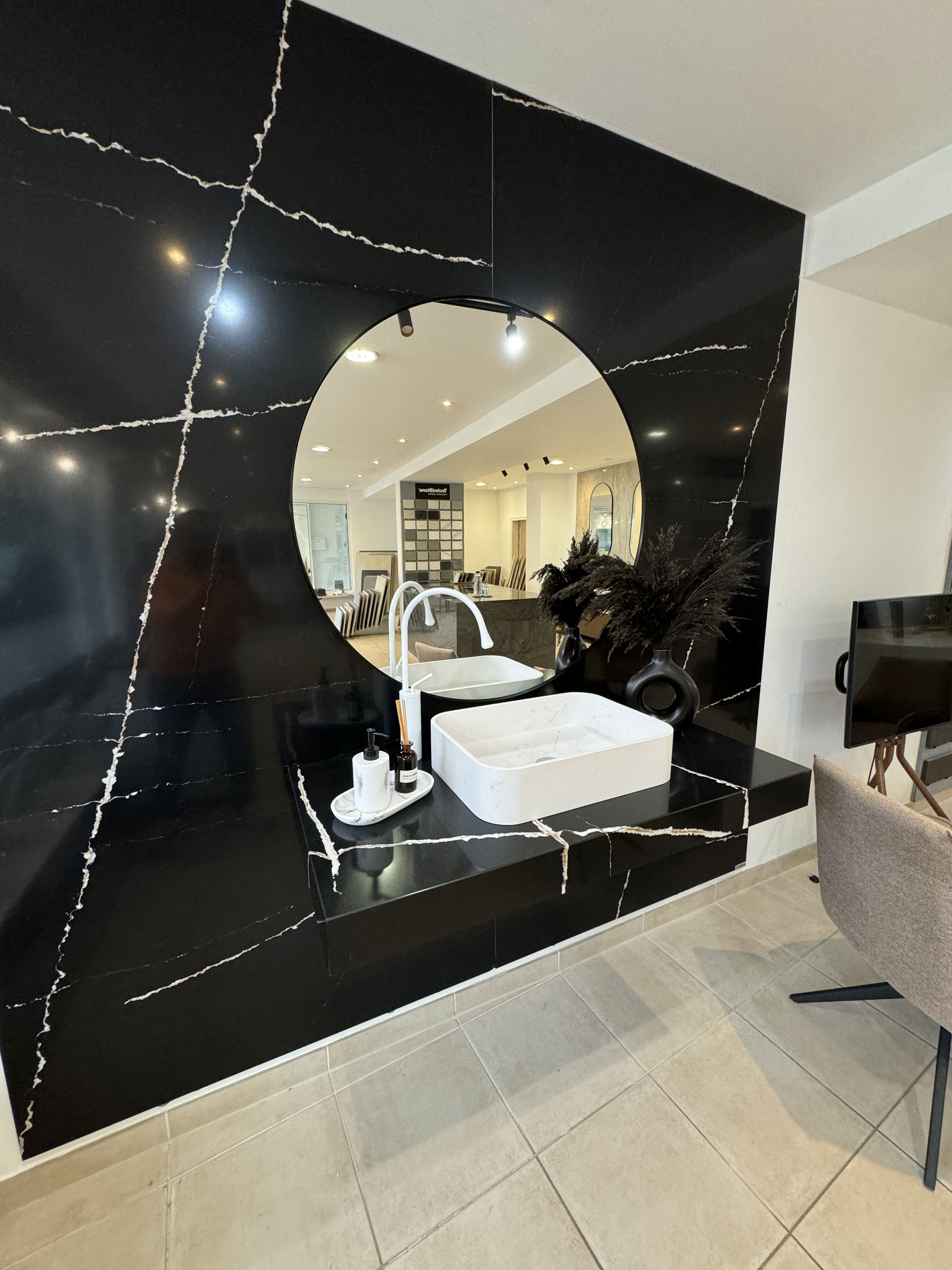Weißes Waschbecken mit Rundspiegel vor glänzender schwarzer Marmorwand mit auffälliger Maserung.