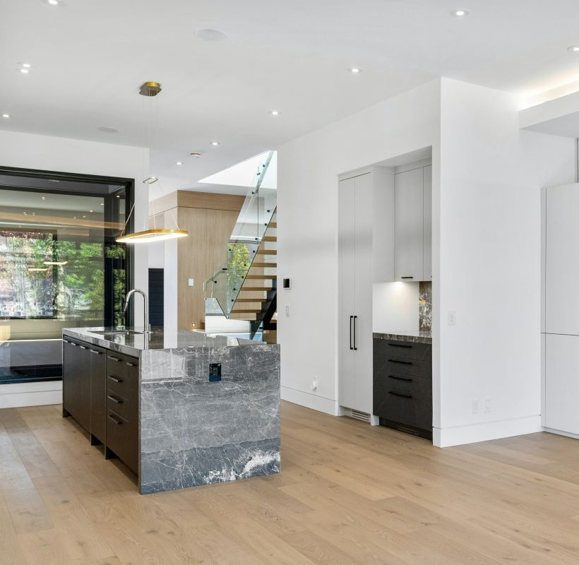 Helles, modernes Wohnzimmer mit offener Küche, Holzfußboden und freitragender Treppe im Hintergrund.