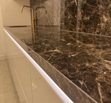 Moderne Küche mit glänzender, dunkel marmorierter Arbeitsplatte und goldfarbenem Wasserhahn vor passender Wandverkleidung.